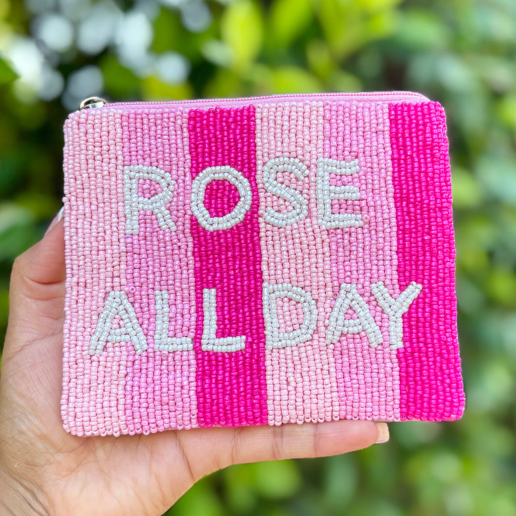 Pink pouch with 'Rose All Day' text held in front of green foliage