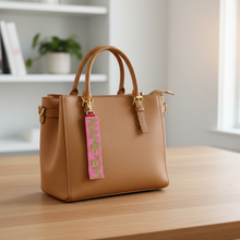 Load image into Gallery viewer, Brown handbag with a pink tag on a wooden surface