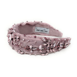 Elegant pink headband adorned with sparkling crystals and gemstones. The luxurious fabric is delicately ruched, creating a sophisticated and glamorous look.
