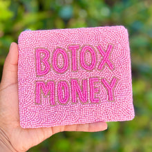 Load image into Gallery viewer, A hand holding a pink beaded pouch with the words 'BOTOX MONEY' embroidered in pink on the front, set against a blurred green outdoor background.