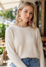 Load image into Gallery viewer, A woman with long blonde hair is wearing a cream sweater and colorful, ornate earrings, standing outdoors with a soft smile and a blurred leafy background.