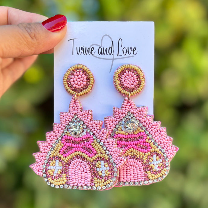 Pink beaded earrings on a card held by a hand with a blurred green background