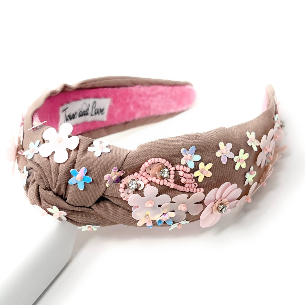 light Brown headband with pink interior, adorned with colorful floral applique and beading. The vibe is playful and feminine, showcasing detailed craftsmanship.