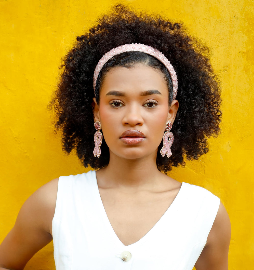 Woman wearing pink ribbon jeweled earrings with a white sleeveless top with a yellow background