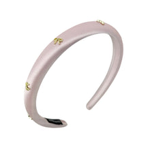 Load image into Gallery viewer, A satin pink headband adorned with small gold embellishments lies on a white background. The delicate design conveys elegance and sophistication.