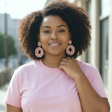 Load image into Gallery viewer, Woman wearing a pink shirt and blue jeans with a blurred outdoor background