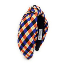 Load image into Gallery viewer, Colorful headband with a plaid pattern in red, blue, and beige hues against a white background. The fabric is knotted in the center, creating a playful and trendy accessory.