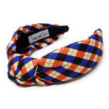 Load image into Gallery viewer, Colorful headband with a plaid pattern in red, blue, and beige hues against a white background. The fabric is knotted in the center, creating a playful and trendy accessory.