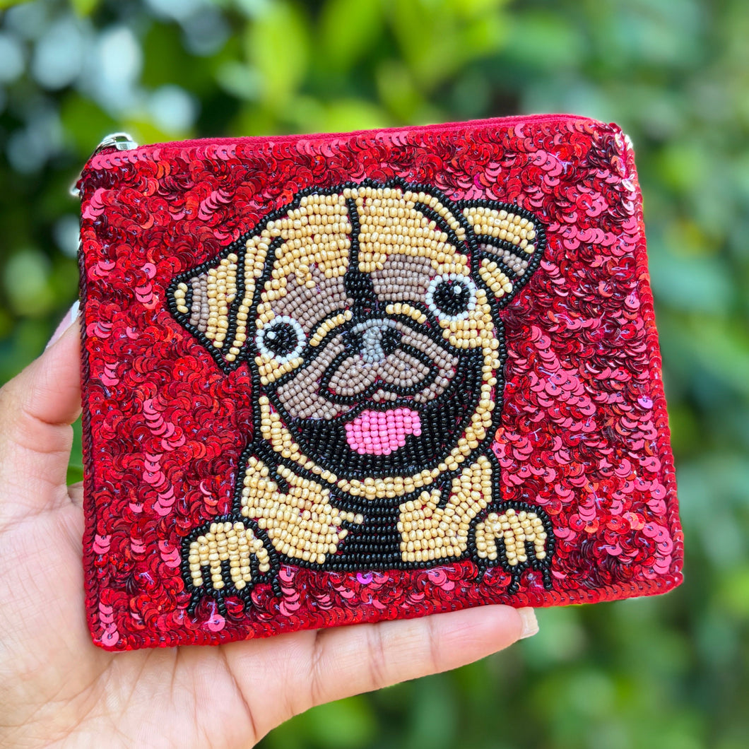 A red sequin pouch features a beaded design of a smiling pug. The dog has its tongue out and front paws visible, adding a playful, cheerful touch.