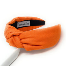 Load image into Gallery viewer, Orange knotted fabric headband worn by a model, featuring a classic wide silhouette and vibrant autumn-inspired color.