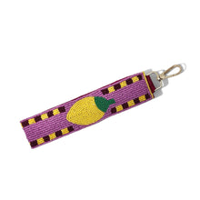 Load image into Gallery viewer, A purple beaded keychain featuring a yellow lemon design with a green stem, attached to a gold metal lobster clasp, shown on a plain white background.