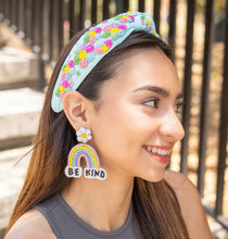 Load image into Gallery viewer, A woman wearing a colorful floral headband and 'BE KIND' rainbow earrings, smiling outdoors.