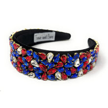 Load image into Gallery viewer, A wide, black headband adorned with vibrant red, blue, and clear gemstones arranged in clusters. The design conveys elegance and boldness.