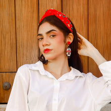 Load image into Gallery viewer, Woman wearing a white shirt, red headband and red nutcracker earrings sitting on steps. 