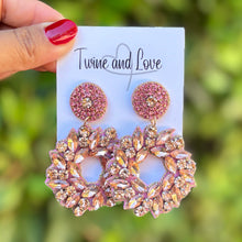 Load image into Gallery viewer, Hand holding a pair of rose gold earrings on a blurred green background