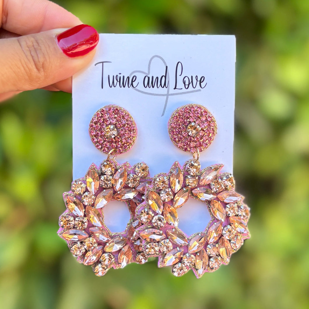 Hand holding a pair of rose gold earrings on a blurred green background