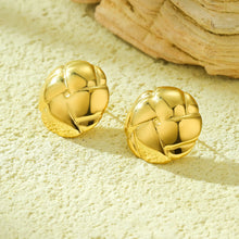 Load image into Gallery viewer, A pair of gold-toned, textured spherical stud earrings resting on a sandy surface with a piece of driftwood in the background.