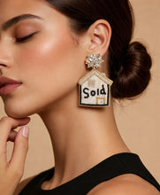 Load image into Gallery viewer, Earring with 'Sold' house design worn by a model on a beige background, Arvin brand visible.