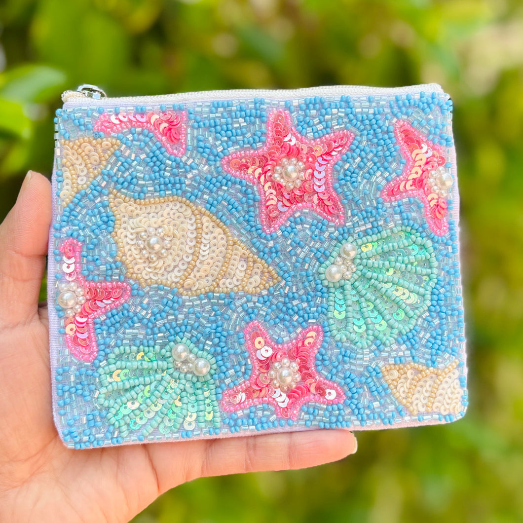 Beaded pouch with a beach theme, featuring colorful starfish and seashell patterns against a blue background. The pouch has a zipper on top.