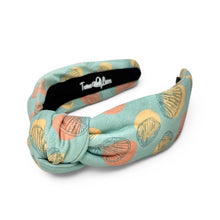 Load image into Gallery viewer, A knotted fabric headband with a mint green background and a pattern of orange, yellow, and black seashell drawings. The inner band  with the brand name 'Twine and Love' printed in white script.
