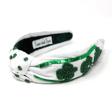 Load image into Gallery viewer, White fabric headband with green sequin clovers and a twisted knot. Inner label reads "Twine and Love." Elegant, festive design.