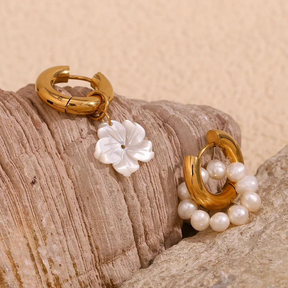 Gold hoop earrings with floral and pearl details on a textured stone surface