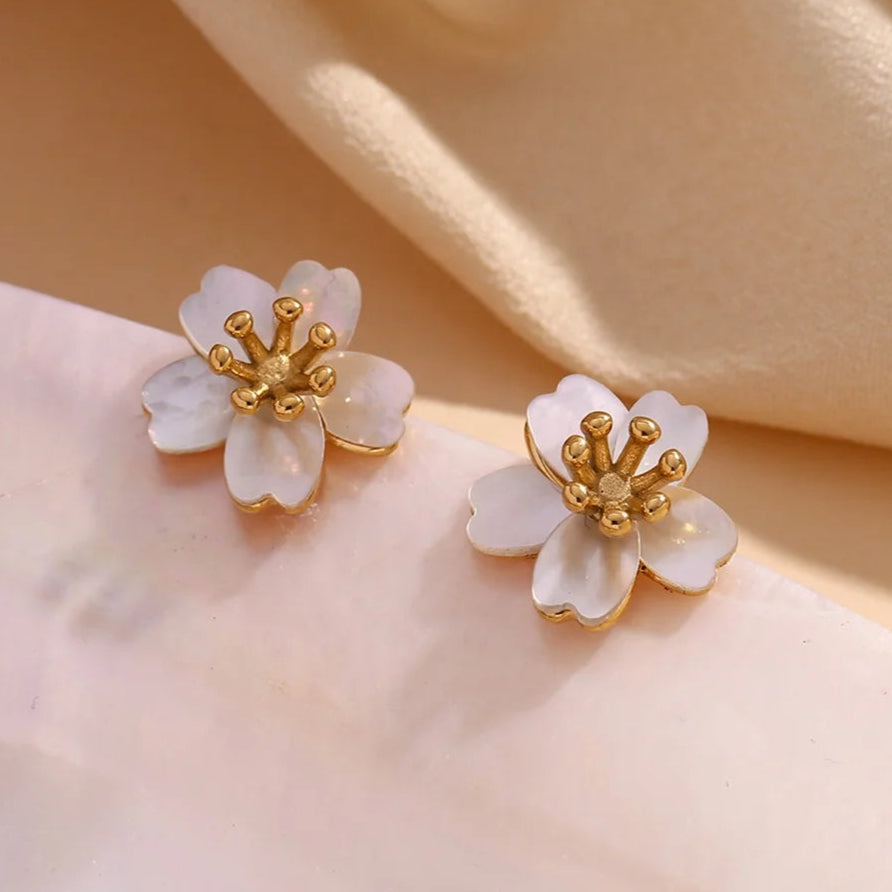 Delicate flower-shaped earrings with white petals and gold center on a white background. They emit an elegant, sophisticated tone.