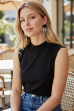 Load image into Gallery viewer, Woman wearing a black sleeveless top and blue jeans with a blurred outdoor background