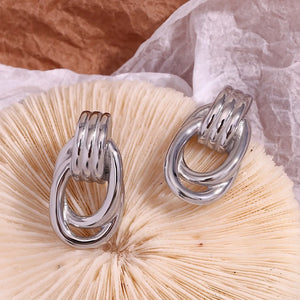 Silver-tone earrings with oval loops and ridged details, resembling linked chains. They convey a modern and elegant style, set against a plain white background.