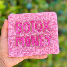 Load image into Gallery viewer, A hand holds a small pink beaded pouch with the words 'BOTOX MONEY' in bright pink lettering, set against a blurred green outdoor background.