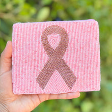 Load image into Gallery viewer, A hand holding a square pink beaded plaque featuring a jeweled pink beaded awareness ribbon, with a blurred green garden background.