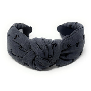 Smokey gray headband with a knotted design, featuring small black bow patterns. The inside tag reads "Time and Love." The tone is stylish and elegant.