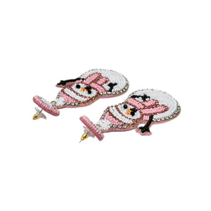 Beaded snowman earrings featuring pink hats and scarves, with black arms and vibrant orange noses. The design conveys a playful, festive tone.