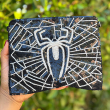 Load image into Gallery viewer, Hand holding a black clutch with white spider design against a green leafy background
