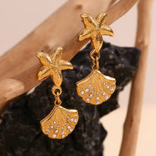 Load image into Gallery viewer, Gold starfish and shell earrings on a wooden stand.