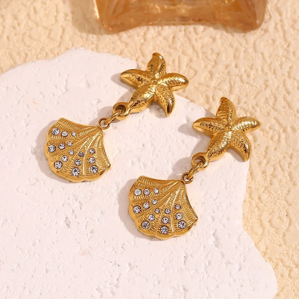 18k Gold Plated earrings feature starfish studs with dangling shell charms adorned with rhinestones, conveying a seaside theme with elegance.