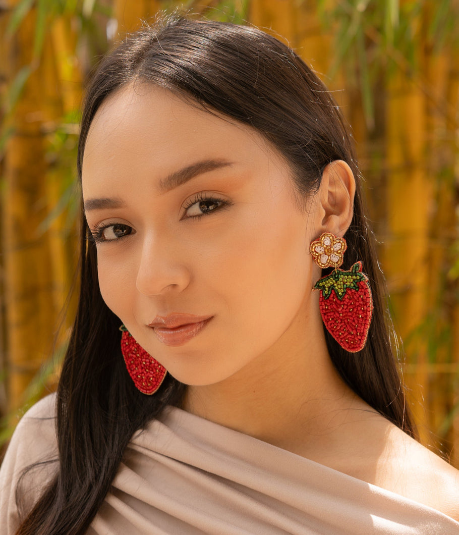 Woman wearing red strawberry-shaped earrings with a blurred natural background