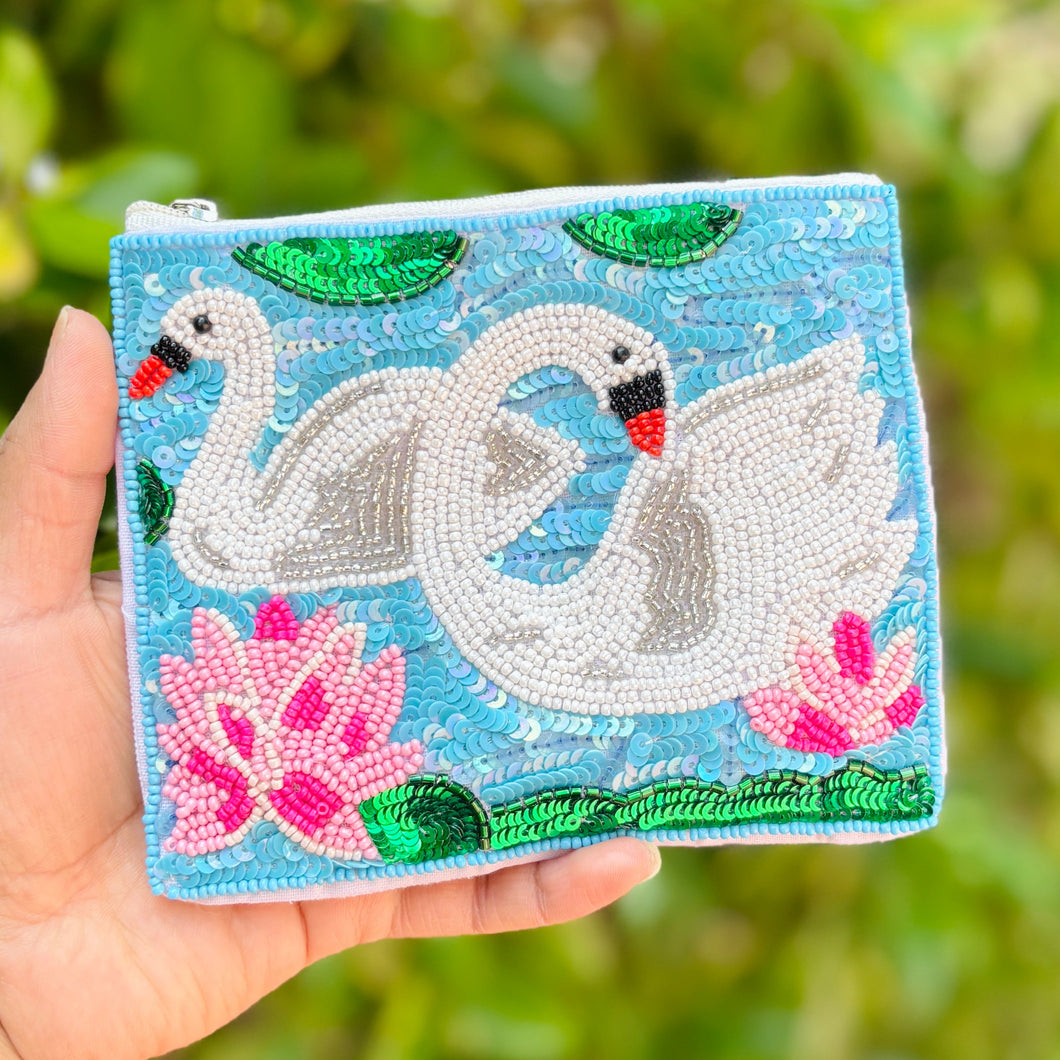 Hand beaded pouch with two white swans, pink flowers, and green leaves on a blue background. 
