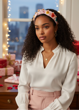 Load image into Gallery viewer, Woman in a white blouse and pink skirt with a valentine headband, standing in a room with decorative lights and gift boxes.