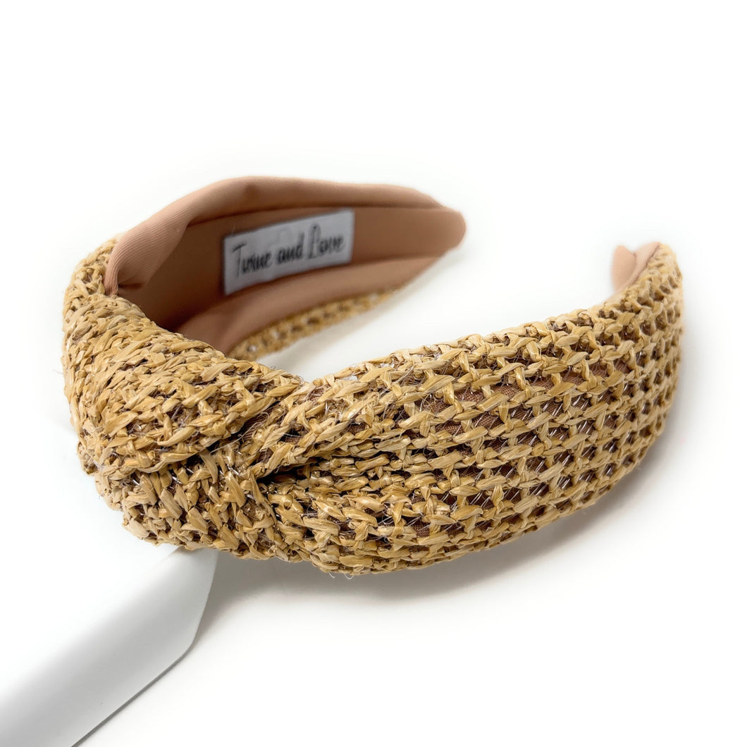 A woven straw headband featuring a twisted knot design, with a soft beige lining. The label inside reads 