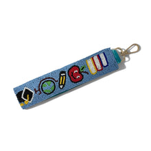 Load image into Gallery viewer, A blue beaded keychain strap featuring colorful symbols representing school subjects (pencils, apple, book, paintbrush, globe, and flag) with a gold metal lobster clasp on a white background.
