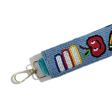 Load image into Gallery viewer, A blue beaded keychain strap featuring colorful symbols representing school subjects (pencils, apple, book, paintbrush, globe, and flag) with a gold metal lobster clasp on a white background.