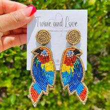 Load image into Gallery viewer, Stylish woman wearing a vibrant yellow floral embroidered headband and colorful tropical parrot statement earrings outdoors.