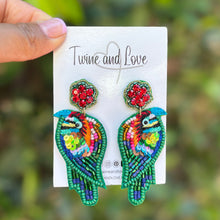 Load image into Gallery viewer, Colorful beaded bird earrings with green trim, rainbow sequin details, and sparkling red crystal floral studs on a white background.