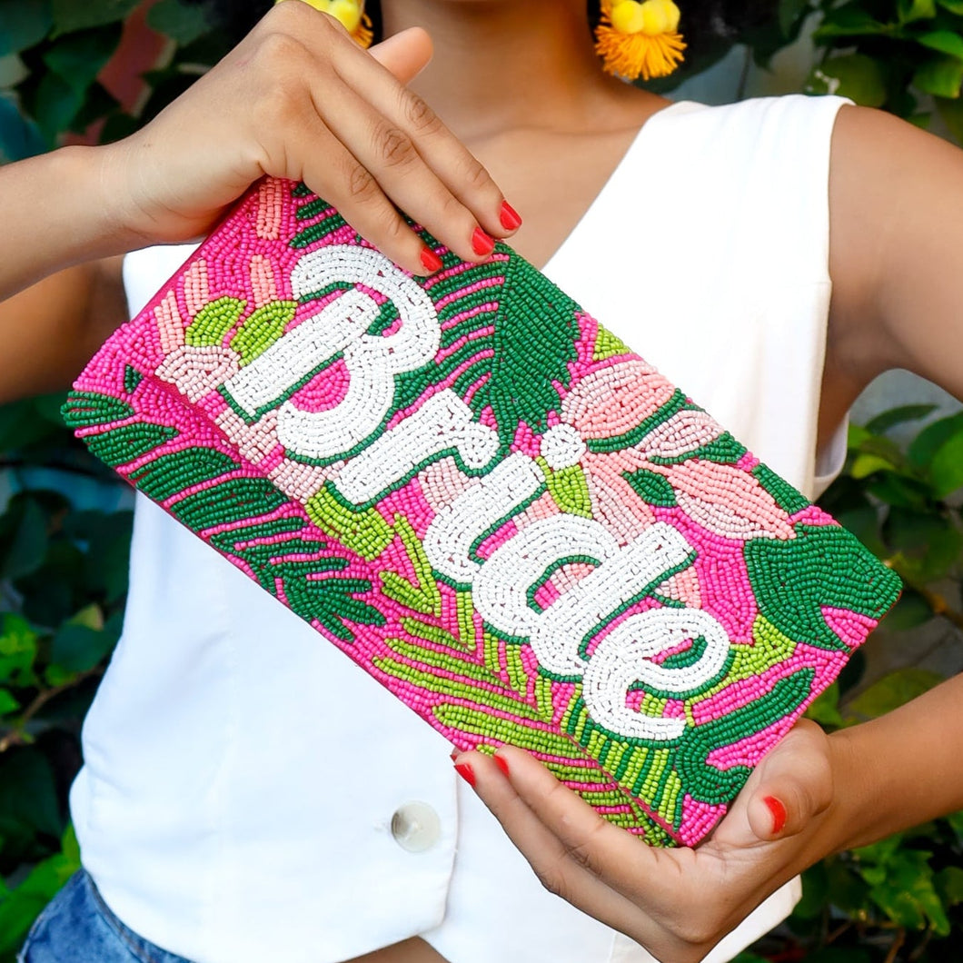 Woman holding a colorful 'Bride' clutch in front of a green leafy background