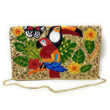 Load image into Gallery viewer, A gold sequined clutch bag featuring a vibrant beaded design of a toucan, parrot, butterflies, and tropical leaves, complete with a gold chain strap, set against a plain white background.