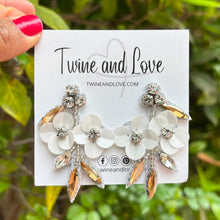 Load image into Gallery viewer, Elegant white floral statement earrings featuring crystal accents, beaded detailing, and champagne-toned gemstones for a feminine glam look.