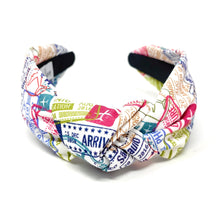 Load image into Gallery viewer, White knotted headband featuring colorful travel-themed passport stamps and airplane graphics on a soft fabric base.