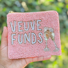 Load image into Gallery viewer, A hand holds a small pink beaded zip pouch outdoors with a blurred green foliage background. The pouch features the words 'VEUVE FUNDS' in white lettering, accompanied by a champagne glass illustration.