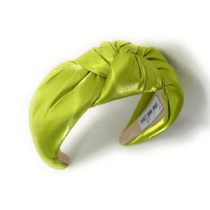 A vibrant green satin headband with a twisted knot design, labeled "Twine and Love" inside. The fabric's sheen adds a touch of elegance.